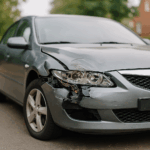 Beschadigde zilvergrijze wagen met ingedeukte zijkant geparkeerd op oprit, gefotografeerd bij daglicht